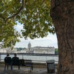 A peaceful scene with two people enjoying the view of London's historic Greenwich Park riverside.